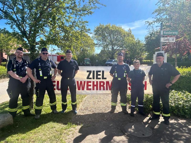 Mehrere Feuerwehrleute stehen vor dem Plakat des Zieles